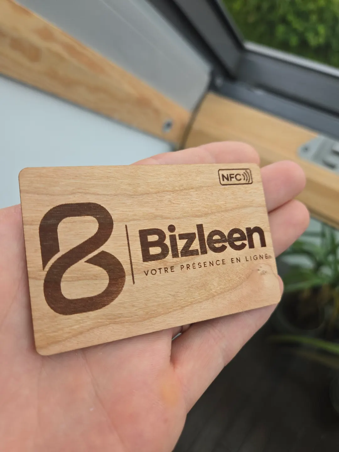 La carte en bois dans la main de Dan, côté recto : le logo Bizleen et le symbole NFC