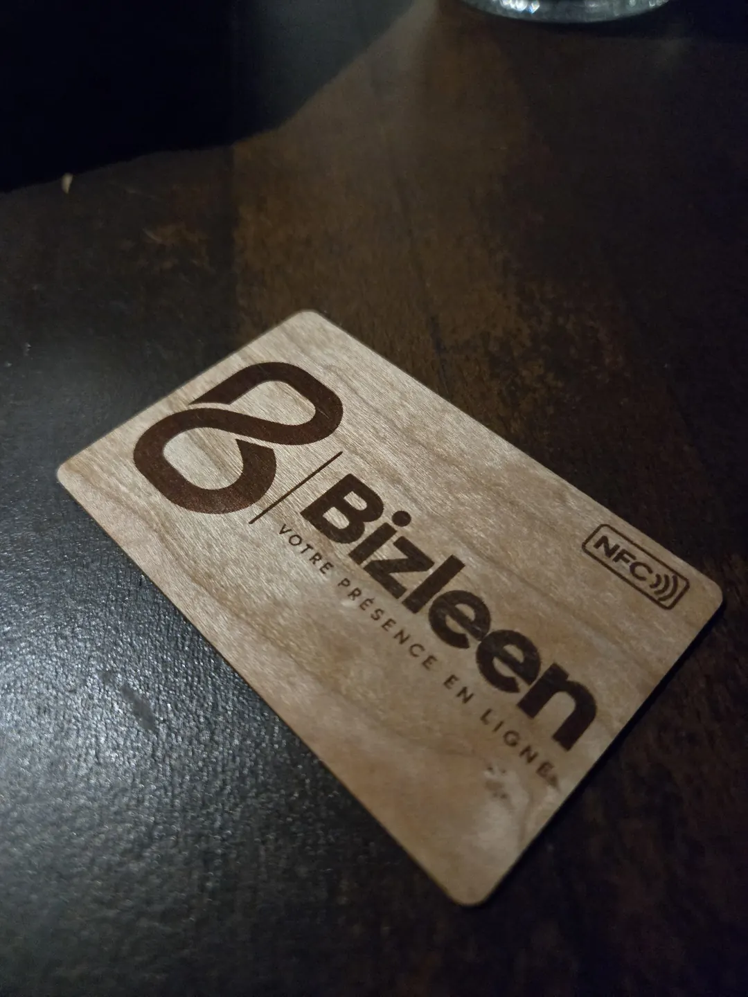 La carte de visite en bois de Bizleen, gravée, posée sur une table sombre